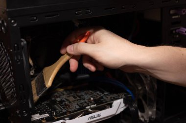 İnsan, bilgisayar sistemi biriminin içinden tozları fırçayla temizler.