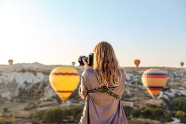 Kadın fotoğrafçı, Kapadokya, Türkiye 'de şafakta uçan sıcak hava balonunun fotoğraflarını çekiyor. Seyahat kavramı.  