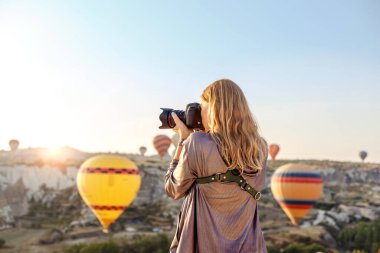 Kadın fotoğrafçı, Kapadokya, Türkiye 'de şafakta uçan sıcak hava balonunun fotoğraflarını çekiyor. Seyahat kavramı.  