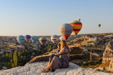 Goreme, Kapadokya, Türkiye 23 Ağustos 2019: Güzel sarışın fotoğrafçı Türkiye 'nin Kapadokya kentinde şafakta uçan sıcak hava balonunun fotoğraflarını çekiyor. Seyahat kavramı.  
