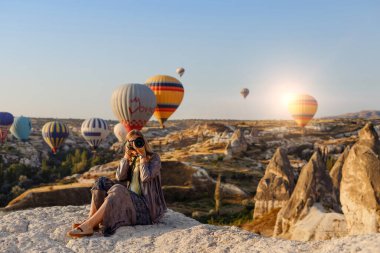 Goreme, Kapadokya, Türkiye 23 Ağustos 2019: Güzel sarışın fotoğrafçı Türkiye 'nin Kapadokya kentinde şafakta uçan sıcak hava balonunun fotoğraflarını çekiyor. Seyahat kavramı.  