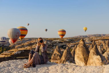 Goreme, Kapadokya, Türkiye 23 Ağustos 2019: Güzel sarışın fotoğrafçı Türkiye 'nin Kapadokya kentinde şafakta uçan sıcak hava balonunun fotoğraflarını çekiyor. Seyahat kavramı.  