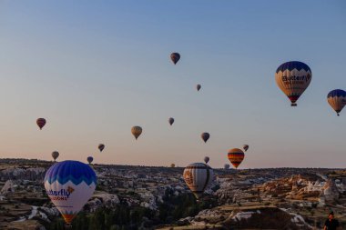 Goreme, Kapadokya, Türkiye 23 Ağustos 2019: Gökyüzünde birçok sıcak hava balonu. İnsanlar onlara yerden bakıyorlar. Kapadokya Dünya Piramitleri. Turizm konsepti.