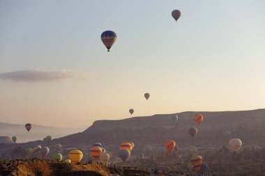 Goreme, Kapadokya, Türkiye 22 Ağustos 2019: Birçok sıcak hava balonu şafakta gökyüzünde uçar. İnsanlar onlara yerden bakıyorlar. Kapadokya Dünya Piramitleri. Turizm konsepti.