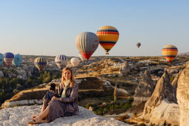 Goreme, Kapadokya, Türkiye 23 Ağustos 2019: Güzel sarışın fotoğrafçı Türkiye 'nin Kapadokya kentinde şafakta uçan sıcak hava balonunun fotoğraflarını çekiyor. Seyahat kavramı.  