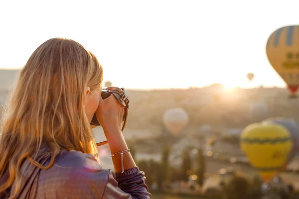 Kadın fotoğrafçı, Kapadokya, Türkiye 'de şafakta uçan sıcak hava balonunun fotoğraflarını çekiyor. Seyahat kavramı.  
