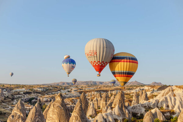 Goreme, Cappadocia, Turkey 23 August 2019: Many hot air balloons in sky. People look at them from the ground. Cappadocia Earth Pyramids. Tourism concept.
