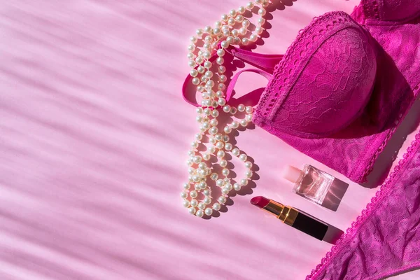 İç çamaşırı sutyeni, iç çamaşırı, parfüm şişesi, ruj ve inci boncuklar. Metin için yeri olan pembe düz bir üst görünüm. Güneş ışınlarıyla çekilmiş bir resim. Kendine dikkat et. Kendini sevmek. Modaya uygun modern kız şeyleri.