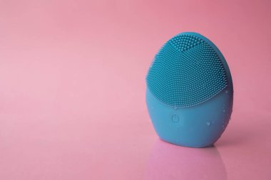 Yüzünü yıkamak için silikon fırça. Pembe arka planda mavi yüz temizleme fırçası. Güzellik ve cilt bakımı. Yüz gerdirme için fırça, yaşlanma önleyici kırışıklıklar ve masaj. Kopyalama alanı ile resim