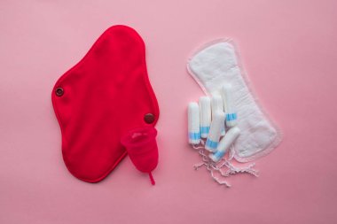 Regl fincanı ve tekrar kullanılabilir adet pedi, tek kullanımlık ped ve tampona karşı. Pembe arka planda düz yatıyordu. Sıfır atık. Çevreye önem vermek. Kadın Sağlığı.