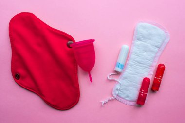 Regl fincanı ve tekrar kullanılabilir adet pedi, tek kullanımlık ped ve tampona karşı. Pembe arka planda düz yatıyordu. Sıfır atık. Çevreye önem vermek. Kadın Sağlığı.