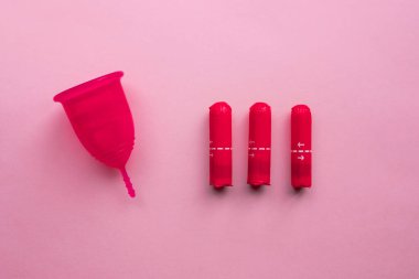 Adet bardağı ve tampon. Tekrar kullanılabilir adet bardağı, tek kullanımlık tamponlara alternatif. Pembe arka planda düz yatıyordu. Sıfır atık. Çevreye önem vermek. Kadın Sağlığı.