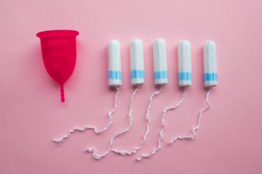 Adet bardağı ve tampon. Tekrar kullanılabilir adet bardağı, tek kullanımlık tamponlara alternatif. Pembe arka planda düz yatıyordu. Sıfır atık. Çevreye önem vermek. Kadın Sağlığı.