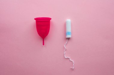 Adet bardağı ve tampon. Tekrar kullanılabilir adet bardağı, tek kullanımlık tamponlara alternatif. Pembe arka planda düz yatıyordu. Sıfır atık. Çevreye önem vermek. Kadın Sağlığı.