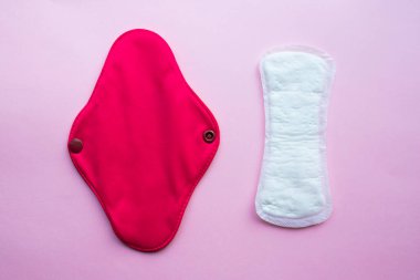 Yeniden kullanılabilir bez hijyenik adet pedi ve tek kullanımlık ped. Pembe arka planda düz yatıyordu. Sıfır atık. Çevreye önem vermek. Kadın Sağlığı. Bilinçli tüketim. 