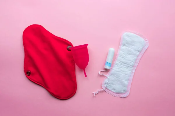 Regl fincanı ve tekrar kullanılabilir adet pedi, tek kullanımlık ped ve tampona karşı. Pembe arka planda düz yatıyordu. Sıfır atık. Çevreye önem vermek. Kadın Sağlığı.