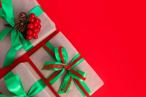 Gifts wrapped in craft paper and decorated with green and red ribbons flat lay on red background. Top view picture with copy space and shallow depth of field