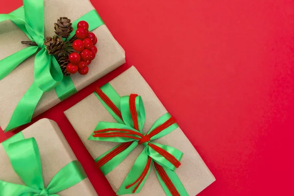 Gifts wrapped in craft paper and decorated with green and red ribbons flat lay on red background. Top view picture with copy space and shallow depth of field