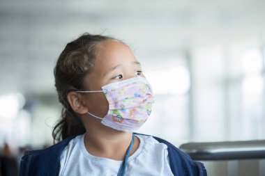 Havalimanında maske takan küçük bir kız ve epidemi sırasında uçakta oturuyor.