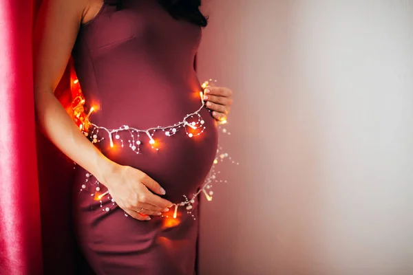 Беременная Женщина Держит Праздничную Гирлянду Возле Живота — стоковое фото