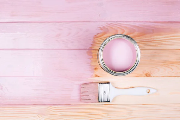 Open can of pink paint with white brush on painting wooden board.