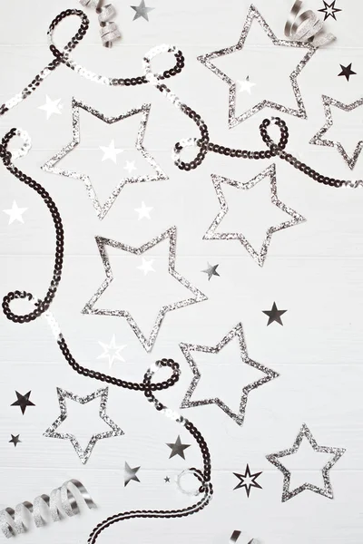 Silver sparkling stars with sequin chain on white wooden background.