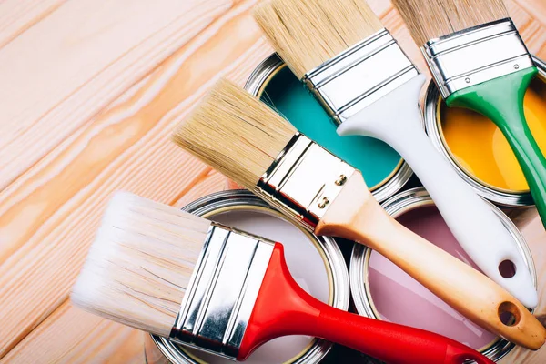 Four open cans of paint with brushes on them on wooden natural background. — Stock Photo, Image