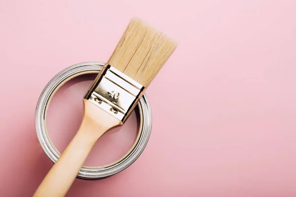 Cepillo con mango de madera en lata abierta de pintura rosa sobre fondo pastel . — Foto de Stock