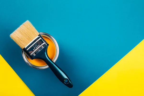 Cepillo en lata abierta de pintura de color amarillo sobre fondo amarillo y azul . — Foto de Stock