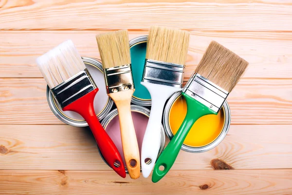 Four open cans of paint with brushes on them on wooden natural background.