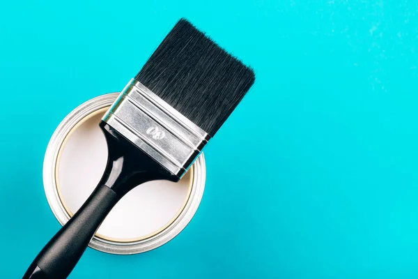 Cepillo con mango negro en lata abierta de pintura blanca sobre fondo azul . —  Fotos de Stock