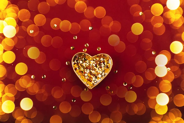 Herzförmige Schachtel mit goldenen Pailletten auf rotem Hintergrund. — Stockfoto