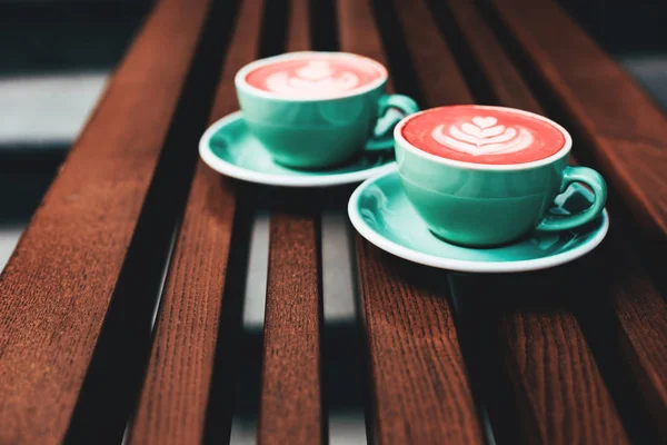 Two cups of Living Coral cappuccino on wooden background. Beautiful foam, greenery ceramic cups. Color of the year 2019