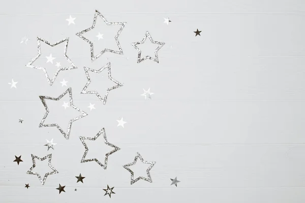 Silver sparkling stars on white wooden background. Festive holiday concept. Place for text