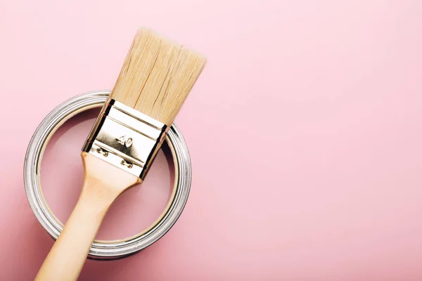 Кисть с деревянной ручкой на открытой банке розовой краски на пастельном фоне . — стоковое фото