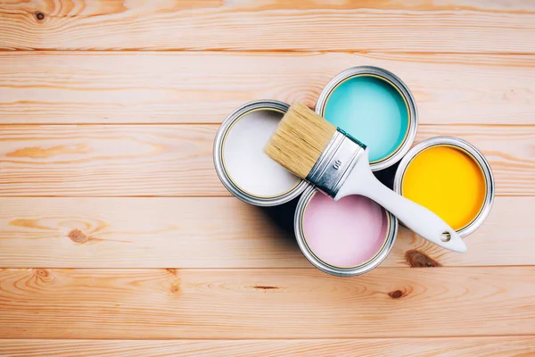 Cuatro latas abiertas de pintura con pincel sobre fondo natural de madera . — Foto de Stock