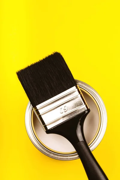 Cepillo con mango negro en lata abierta de pintura sobre fondo amarillo . —  Fotos de Stock