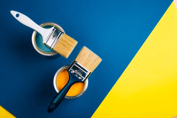 Two open cans with brushes on them on yellow and blue background. — Stock Photo, Image