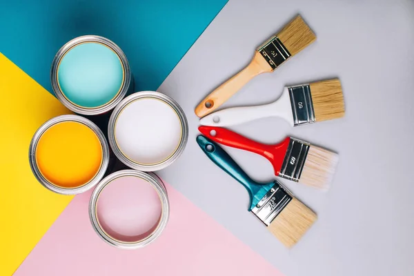 Four open cans of paint with brushes on bright background.