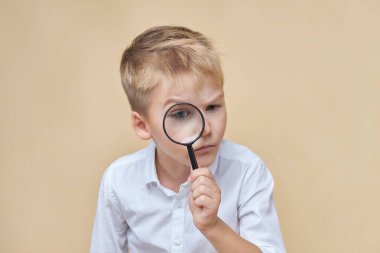 Meraklı çocuk büyüteçle aşağıdaki şeye bakıyor..