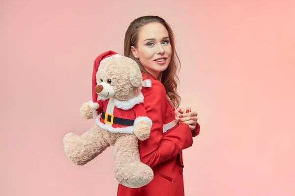 Uzun dalgalı saçlı genç bir kadın Noel Baba kılığında oyuncak bir ayıyı öpüyor. Yeni yıl konsepti.