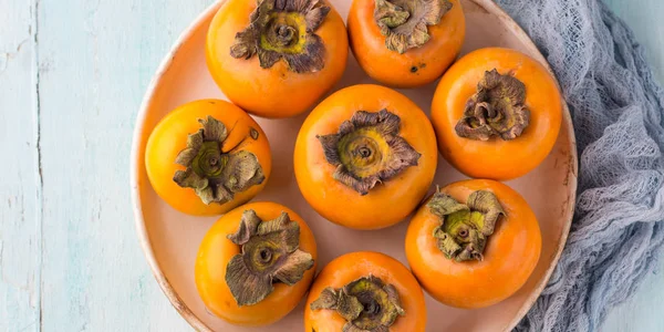 Ripe persimmons on turquoise background — Stock Photo, Image