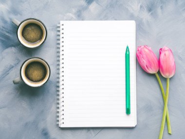 İki kahve fincanı ve kalem ve gökyüzü mavi Lale ile boş Not Defteri sayfası arka plan boyalı. En az düz lay