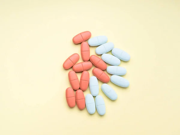Niebieskie i czerwone tabletki na żółtym tle — Zdjęcie stockowe