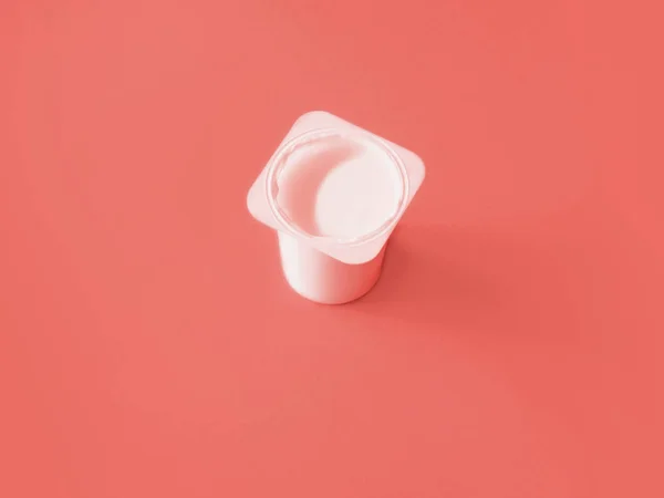 Plain yogurt in plastic glass on monochrome coral