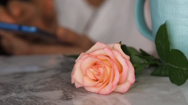 Rosa en la mesa de mármol y la mujer con teléfono detrás — Vídeos de Stock