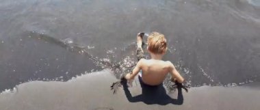 Küçük çocuk kıyıda siyah kum ile oynuyor