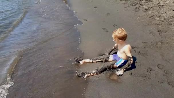 Mały chłopiec gra z czarnym piaskiem na brzegu — Wideo stockowe