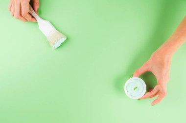 Yeşil arkaplanda boya fırçası olan el.