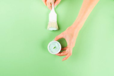 Yeşil arkaplanda boya fırçası olan el.